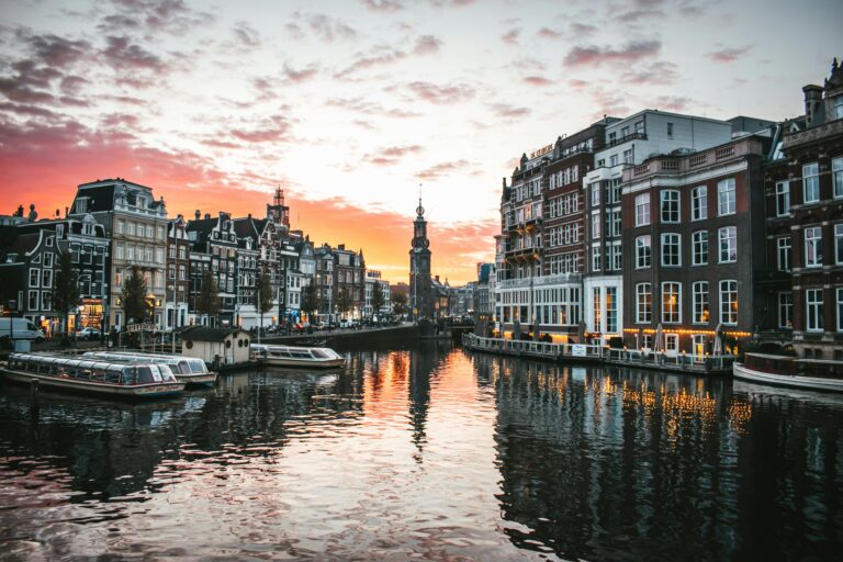 Sunset over a canal in Amsterdam with historic waterfront buildings and tour boats.